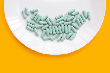Blue capsules in white plate on yellow background.