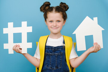Portrait of happy schoolgirl holds white hashtag sign and house model, label for business, wears...