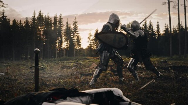 Dark Age Battlefield: Brutal Fight to Death of Two Armored Medieval Knights, Killing Enemy with Sword. Battle of Armed Warrior Soldiers in Forest. Cinematic Smoke, Mist, Light in Historic Reenactment