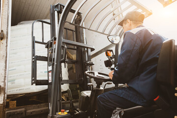 A man on a forklift works in a large warehouse, unloads bags of raw materials
