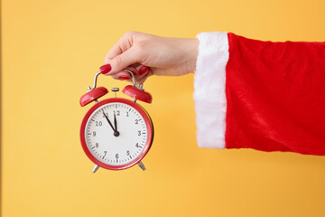 Red alarm clock holds hand in santa claus costume closeup