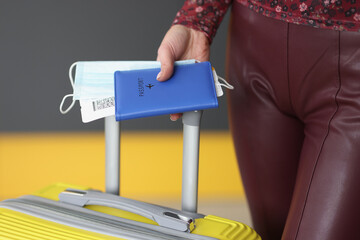 Woman holding passport, plane ticket, medical mask and suitcase