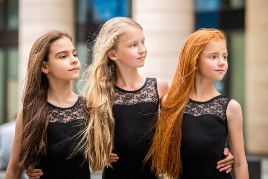 Three teenage girls with loose hair blonde redhead and brunette, stand in profile outside in summer. Vloses develop in wind.