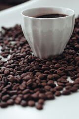 Cup of hot black coffee standing on fresh aromatic roasted coffee beans isolated on white background. Vertical