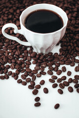 Cup of hot black coffee standing on fresh aromatic roasted coffee beans isolated on white background. Vertical