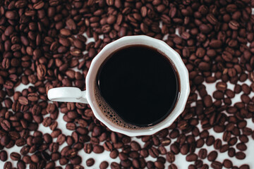 Cup of hot black coffee standing on fresh aromatic roasted coffee beans