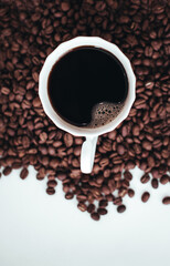 Cup of hot coffee standing on fresh aromatic roasted coffee beans isolated on white background. Vertical