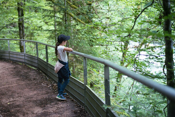 Naklejka na ściany i meble The girl on the terrace admires the forest landscape. Walk in the woods.