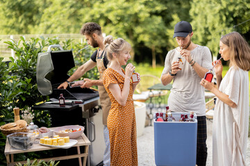 Happy friends hang out on a picnic, grilling food and standing with alcohol drinks at backyard on nature