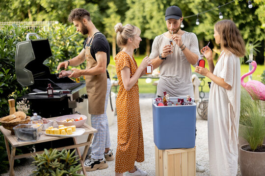 Happy Friends Hang Out On A Picnic, Grilling Food And Standing With Alcohol Drinks At Backyard On Nature