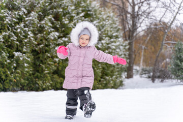 playful child girl in pink coat having fun in winter park
