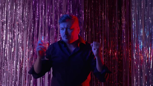 Night club party. Drunk man. Festive celebration. Funny guy dancing with glass of champagne shadow light interior on shimmering colorful cascade curtain.