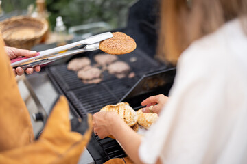 Friends grilling meat and buns for a burger on a gas grill outdoors, close-up