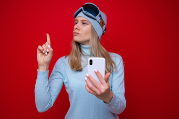 Portrait of a young woman in a sweater and ski goggles with a phone