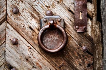 Heavy rusty iron door knocker, ring in front of rectangular iron plate on weathered grained massive...