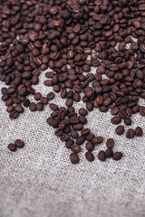 Fresh aromatic roasted coffee beans scattered on a beige burlap background. Vertical. Top view