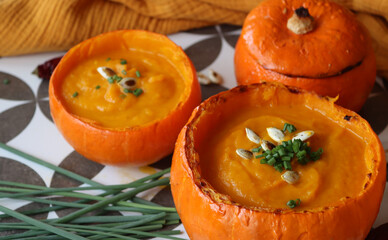 Creamy, nourishing butternut squash soup with a hunk of crusty bread. Fall comfort food. Healthy eating concept. Top view photo of beautiful orange soup served in a squash bowl. 
