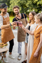 Young friends have fun, hanging out together with alcohol drinks in glasses at picnic outdoors. People spending summer time and celebrating at backyard