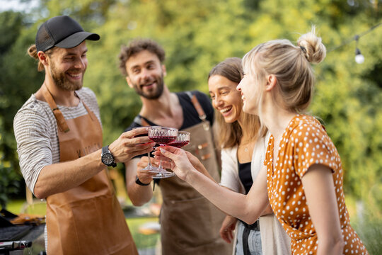 Young friends have fun, hanging out together with alcohol drinks in glasses at picnic outdoors. People spending summer time and celebrating at backyard