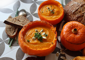 Creamy pumpkin soup and homemade bread on grey tiled table. Soup in a squash top view photo. Thanksgiving menu ideas.  
