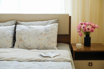 Close up shot of bedroom full of natural light with nightstand, a book and bouquet of ranunculus in a glass vase near the bed. Good morning concept. Copy space for text, background, top view.
