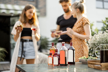 Young people celebrate and have fun, drinking alcohol drinks at backyard. Bottles with blank labels on the table on the foreground