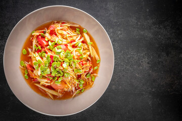 Som Tum, Som Tam, Thai E-San food, spicy papaya salad with pickled fish, tomato, lime and chilli topping with phatakin seed on dark tone texture background, top view