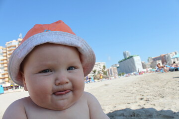 cute little toddler boy in orange hat playing on the beach in summer