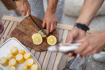 Two men preparing fresh fish for grilling, seasoning it with lemon and spices at table outdoors, close-up