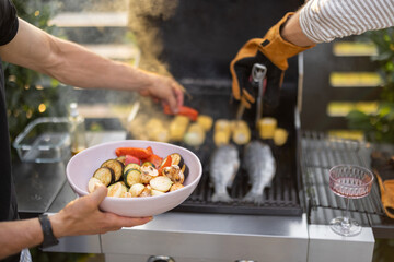 People grilling fish and corn on a modern grill outdoors at sunet, close-up. Cooking food on the open air