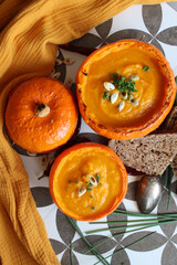 Creamy, nourishing butternut squash soup with a hunk of crusty bread. Fall comfort food. Healthy eating concept. Top view photo of beautiful orange soup served in a squash bowl. 
