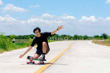 A young Asian man is wearing a black shirt and pants. play skateboard Show the posture of a turn around. On a country road on a sunny day with sky. Looking at the camera, Play surf skate.