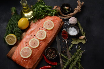 Fresh raw salmon fish fillet with spices and lemon slices over dark stone background