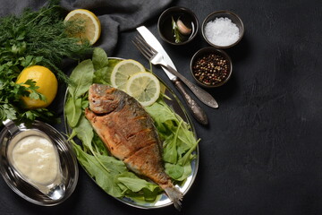 Fried fish dorado with fresh herbs and lemon on silver tray