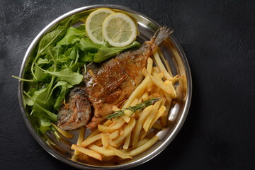 Fried fish dorado with potatoes chips, fresh herbs and lemon