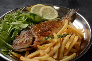 Fried fish dorado with potatoes chips, fresh herbs and lemon