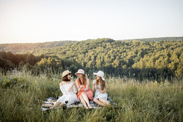 Three stylish happy female friends having fun on outdoor picnic party, eating tasty gourmet french...