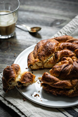 Cinnamon swirl yeast cake on white plate and glass of coffee on dark wooden table.