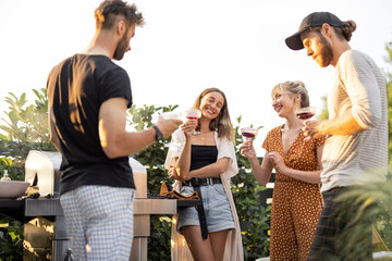 Young friends having fun at picnic outdoors, talk and drink wine at the backyard on a sunset....