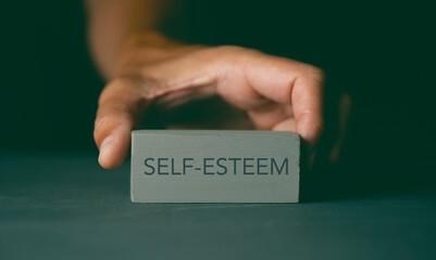 man showing a toy block with the text self-esteem