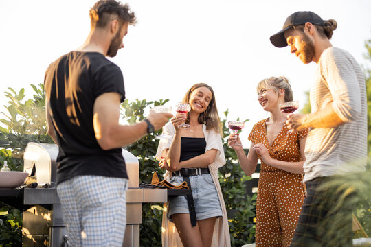 Young friends having fun at picnic outdoors, talk and drink wine at the backyard on a sunset. Spending summer time in a small group on the open air