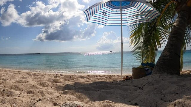 Spiaggia tropicale con un ombrellone vicino ad una palma in riva al mare nell'isola di Cozumel in Messico. Nello sfondo cielo blu e barche in navigazione