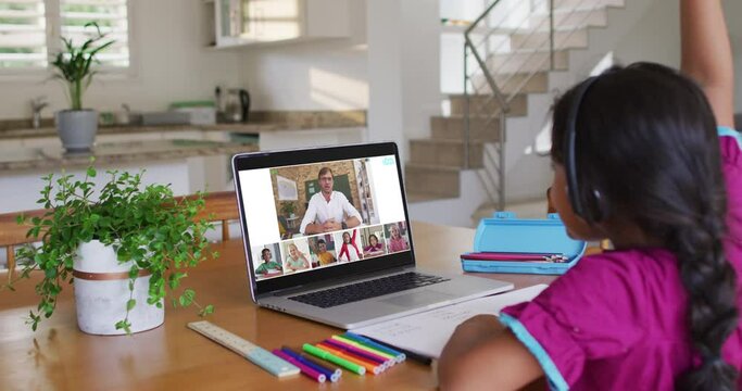 Schoolgirl using laptop for online lesson at home, with diverse teacher and class on screen