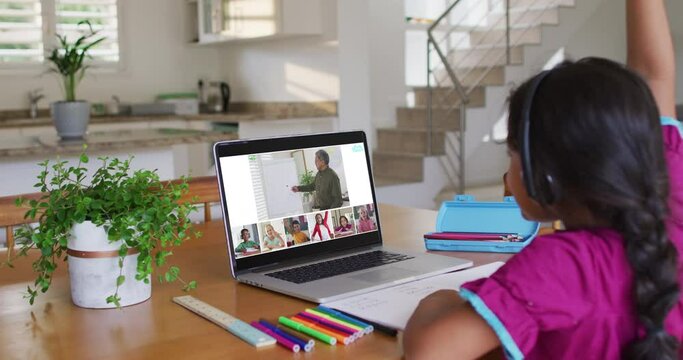 Schoolgirl using laptop for online lesson at home, with diverse teacher and class on screen