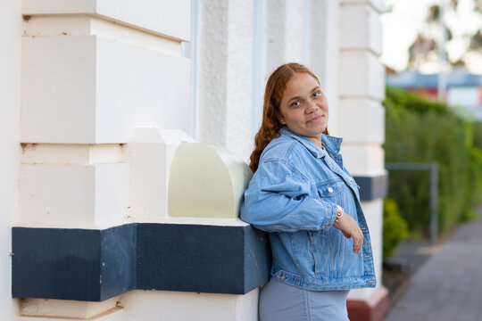 young lady in denim jacket with back to wall looking at camera