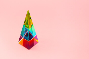 Rainbow glass pyramid prism on pink background with copy space, horizontal