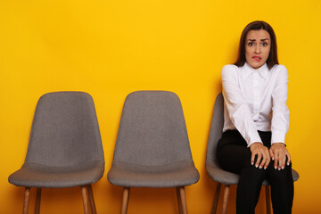 Cute stylish modern brunette woman is sitting on the chairs line on job interview appointment