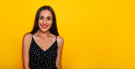 Happy excited gorgeous smiling brunette woman in a black summer dress is posing isolated on yellow background and having fun