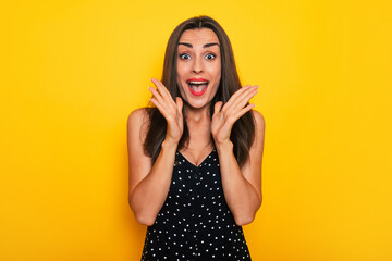 Happy excited gorgeous smiling brunette woman in a black summer dress is posing isolated on yellow background and having fun