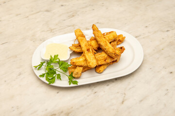 Chopped aubergines like fried fingers in tempura with dip sauce and fresh parsley on a white plate.